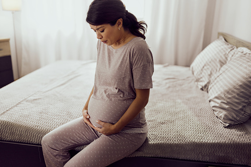 Worried pregnant woman holding her stomach while having contractions on a bed in the morning. Copy space.