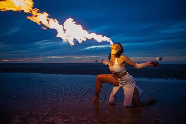 Beautiful brunette female fire eater on the beach at night