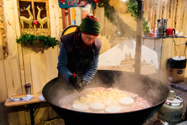 cuisson de la tartiflette, un plat traditionnel français de pommes de terre festonnées, bacon et fromage, dans un grand chaudron pendant le marché de noël de montreux, suisse - swiss culture photos et images de collection
