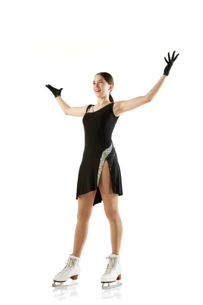 wow, success, win. happy young girl, female figure skater in black stage costume standing with raising hands isolated over white background. sport, beauty, winter sports - axel imagens e fotografias de stock