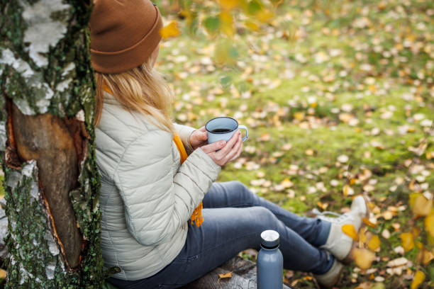 istock Woman drinking hot drink and resting on bench in forest 1447114844