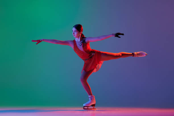 young sportive girl, junior female figure skater in red stage costume skating isolated over gradient green-blue background in neon light. grace, beauty, winter sports - axel imagens e fotografias de stock