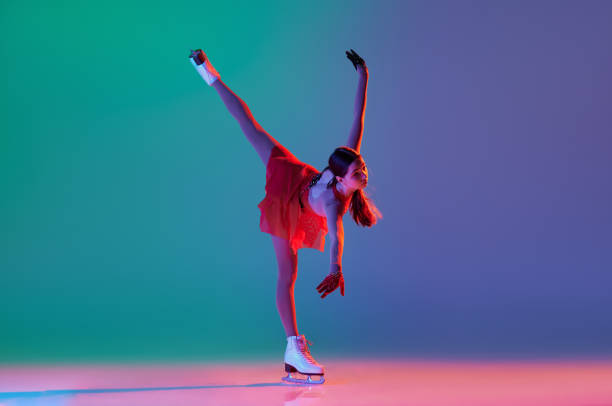 joven deportista, patinadora artística femenina junior con traje de escenario rojo patinando aislada sobre fondo verde-azul degradado en luz de neón. gracia, belleza, deportes de invierno - axel fotografías e imágenes de stock