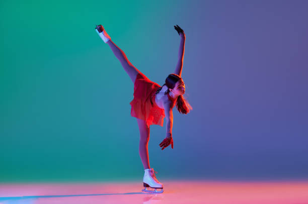 young sportive girl, junior female figure skater in red stage costume skating isolated over gradient green-blue background in neon light. grace, beauty, winter sports - axel imagens e fotografias de stock