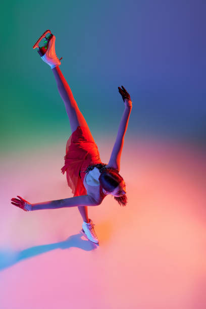 vista aérea de una adolescente deportiva, patinadora artística femenina junior en traje de escenario rojo patinando aislada sobre fondo verde-azul degradado en luz de neón. gracia, belleza, deportes de invierno - axel fotografías e imágenes de stock