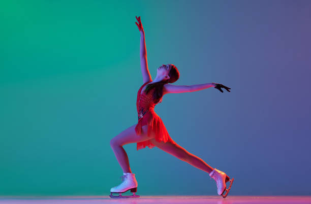 deportes de invierno. una patinadora artística femenina junior con traje de escenario rojo que muestra elementos de patinaje artístico base, movimientos aislados sobre fondo verde-azul degradado en luz de neón. - axel fotografías e imágenes de stock