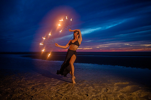 Beautiful brunette female fire dancer on the beach at night
