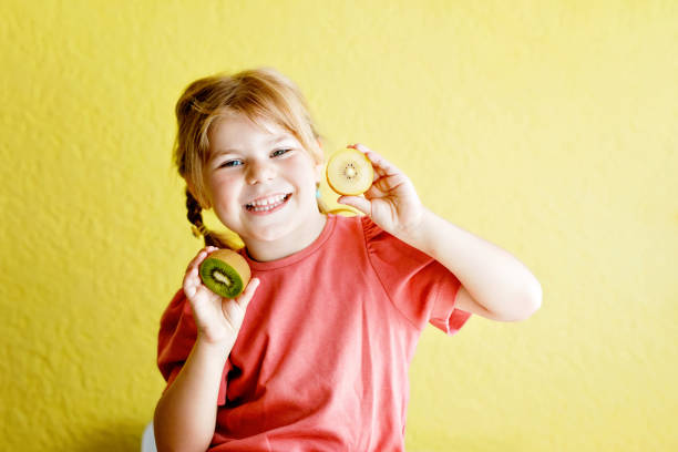 Happy little child girl with yellow and green kiwi fruits on yellow background. Preschool girl smiling. Healthy fruits for children Happy little child girl with yellow and green kiwi fruits on yellow background. Preschool girl smiling. Healthy fruits for children. mini kiwi stock pictures, royalty-free photos & images
