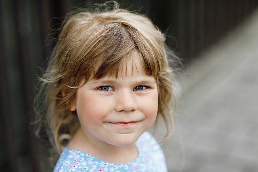Portrait of happy smiling toddler girl outdoors. Little child with blond hairs looking and smiling at the camera. Happy healthy child enjoy outdoor activity and playing