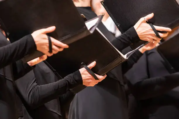 Detail of human hands holding sheet music while singing in choir