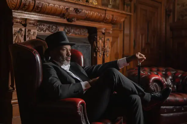 A handsome elegant 1920s style black gentleman in a luxury drawing room with a chesterfield sofa