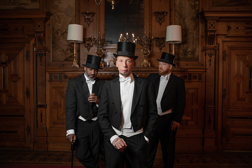 Three handsome 1920s style gentlemen wearing white tie and top hat in a luxury brown bar