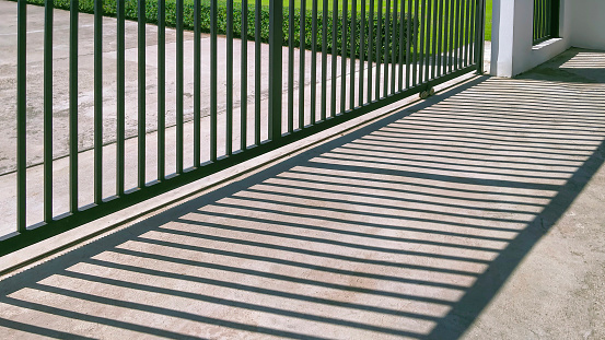 Sunlight and shadow on surface of automatic sliding metal fence gate in front of modern house, perspective side view with copy space