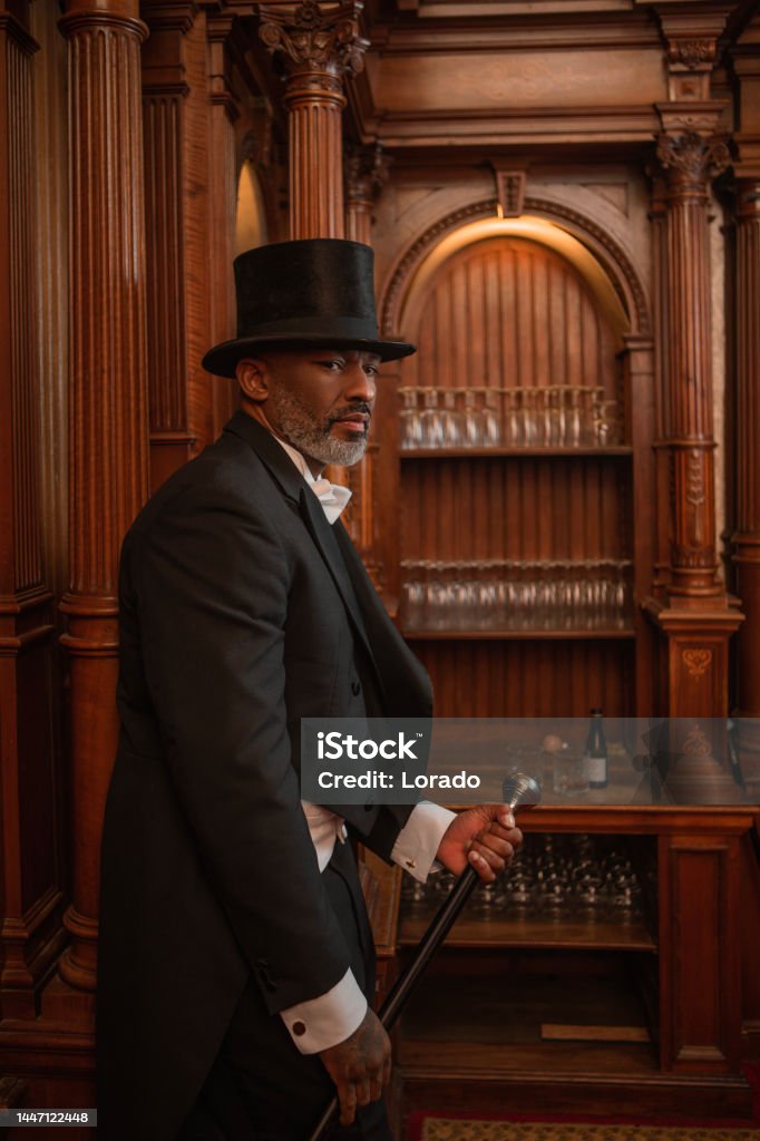 A handsome elegant 1920s style black gentleman in a brown bar A handsome elegant 1920s style black gentleman wearing white tie and top hat in a luxury brown bar Bar - Drink Establishment Stock Photo