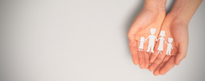 Family care concept. Hands with paper family silhouette on table.