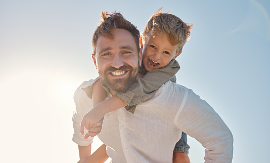 Family, portrait and father and son relax against a blue sky background, playing and having fun outdoors. Happy family, travel and child embracing dad in nature, laughing and enjoying summer together