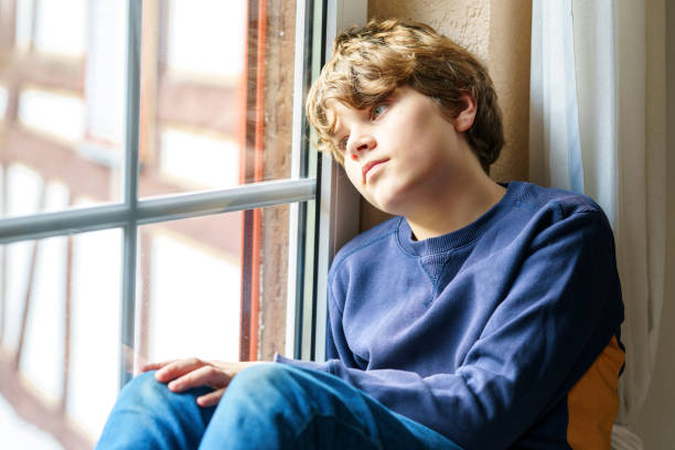 istock Sad pretten kid boy sitting on window. Unhappy angry child 1447125540