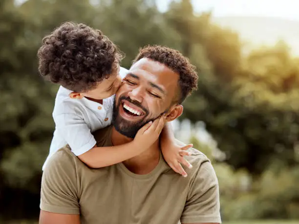 Photo of Father, bonding kiss and boy child hug happy in nature with quality time together outdoor. Happiness, laughing and family love of a dad and kid in a park enjoying nature hugging with care and a smile