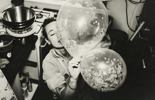 Portrait of young casual woman in her kitchen. She plays with the balloons of a birthday party.