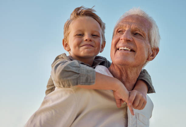 piggyback, bambino e nonno con il sorriso nella natura per la libertà, l'amore e il relax con un cielo blu. ritratto di un bambino giovane, felice e giocoso che è divertente, legato e pazzo con un uomo anziano nel parco - family summer portrait nature foto e immagini stock