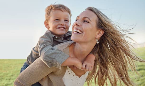 madre, bambino e piggyback felice in estate, vacanza e cielo blu, sole e giocare in un parco verde. mamma, bambino e sorriso felici che si divertono all'aperto per le vacanze con sorriso, risate e amore nella natura - attrezzatura per giochi allaperto foto e immagini stock