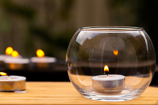 An image showing decorative miniature candles, one inside a glass bowl and others outside on a timber tabletop, ideal as a relaxation theme or mood.