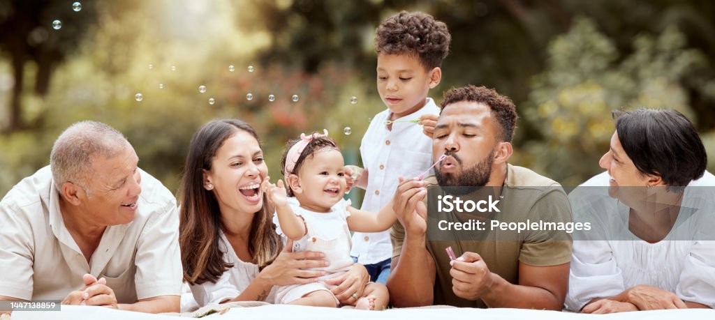 Happy, smile and big family blowing bubbles in a garden on a summer picnic in Puerto Rico. Happiness, grandparents and parents with children playing, having fun and relaxing together in the park Family Stock Photo
