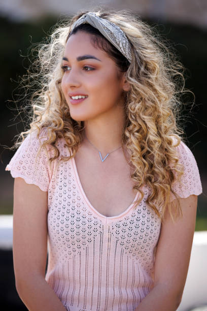 Portrait of beautiful teenage girl with blond curly hair, wearing headband and pastel pink blouse stock photo