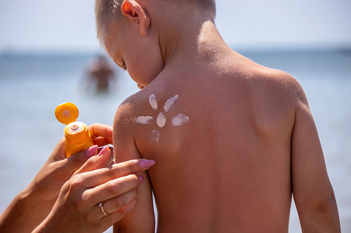 Sunscreen on the child's face and back. On the background of the sea. Selective focus
