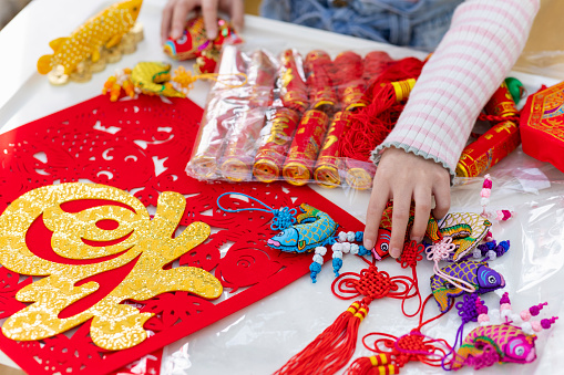 A close-up shot of an unrecognisable young girl crafting decorations at a table for Chinese New Year, ready to decorate the home in Newcastle Upon Tyne, England. Patterned imitation fire crackers used to scare away evil spirits are laid out and ready to be hung up as well as patterned fish ornaments which symbolise wealth and prosperity coming into the new year.