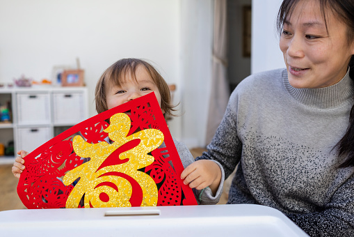 A mother and her young boy have crafted a patterned red paper cutting in their living room for Chinese New Year at their home in Newcastle Upon Tyne, England. The patterned red paper cuttings bring luck and happiness coming into the new year and the red symbolises the springtime coming.