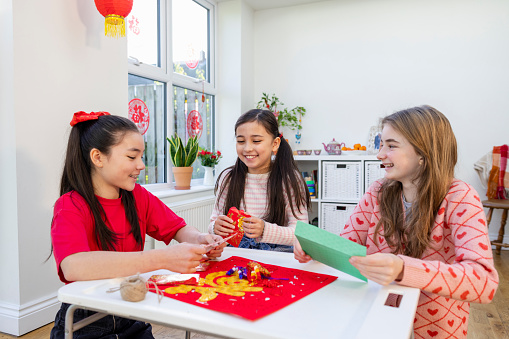 A shot of three young girls crafting decorations in the living room for Chinese New Year at a home in Newcastle Upon Tyne, England. Preparations are beginning to celebrate with the whole family.
