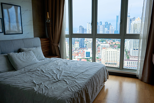 a made-up bed near a huge window overlooking the city center.