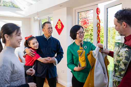 A shot of a woman greeting her family that are visiting her home in Newcastle Upon Tyne, England to celebrate Chinese New Year together. The home has traditional Chinese New Year decor and they have brought a gift, a bouquet of white orchids which symbolises good fortune.