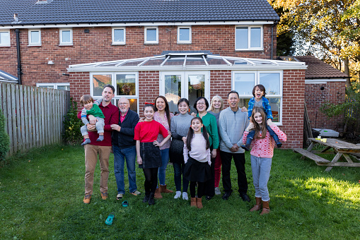 A front-view portrait shot of a large family standing together smiling and looking at the camera in a garden at a home in Newcastle, England.
