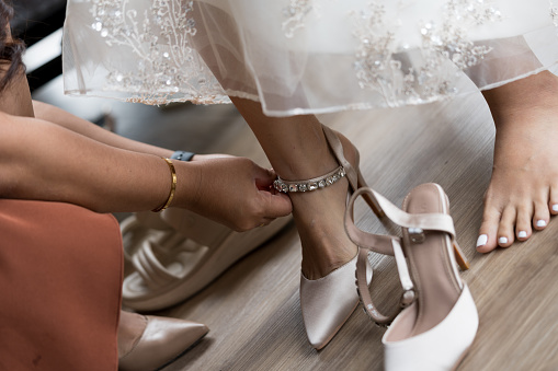 Bridesmaid helping bride put on shoe. Modern bridal style.