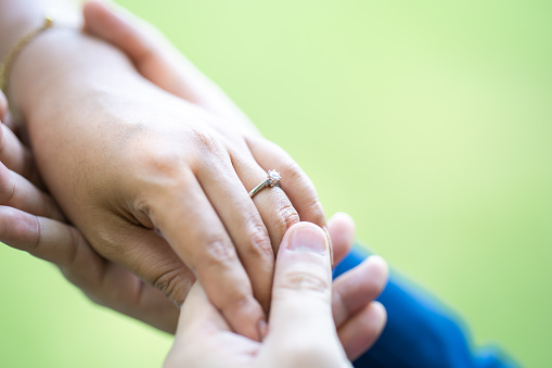 A man is wearing a wedding ring to a woman on his left ring finger. Close up on the hand in the outdoor field with the sunlight and tree shadow shading.