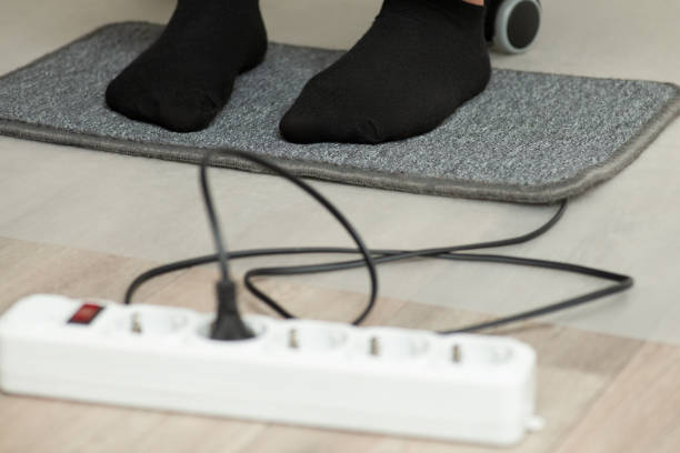 Feet of a person in black socks stand on small carpet, which is being warming by electric power stock photo