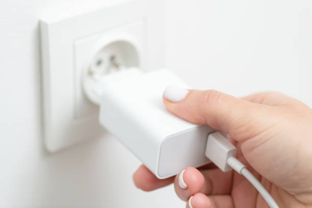 istock Female hand inserts charging device into electrical outlet, close up 1447151845