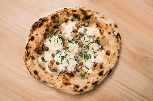 Top view of Neapolitan pizza: Stir-fried Swiss mushrooms topped with special truffle sauce pizza, Served on a white plate on a wooden table. Italian fresh baked Napoli pizza.