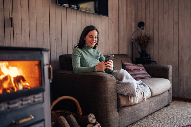 istock Smiling girl covered in a blanket, sitting on the sofa, using her mobile phone. 1447152151