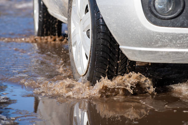 Close up shot of car wheels in puddle on sunny spring day during thaw stock photo