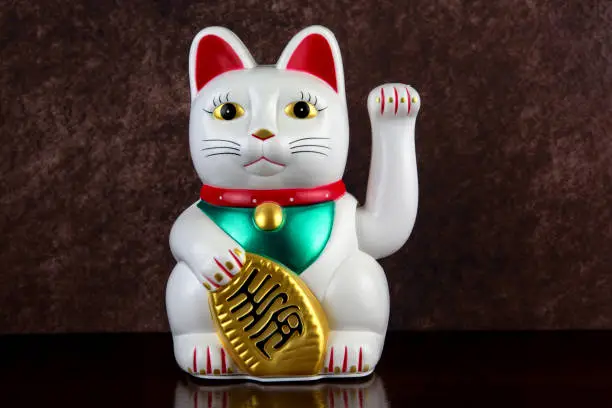 White beckoning maneki neko lucky cat on a varnished wooden shelf