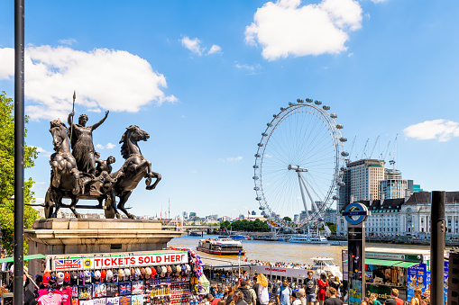 London, United Kingdom - June 22, 2018: Westminster pier ticket kiosk for boat tour on Thames river, Millennium eye wheel, Boudiccan rebellion statue