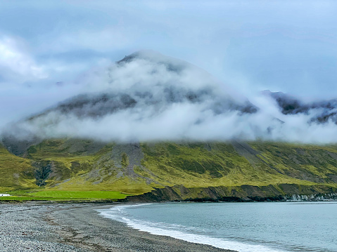 Mountain over the sea. The peak of the mountains is hidden in the clouds and fog. Foggy weather. Cold climate.