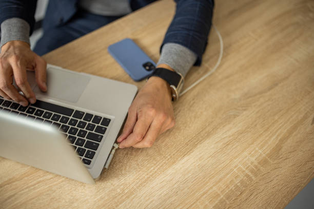 istock Businessman plugging In charging cable into laptop while working in office 1447158673