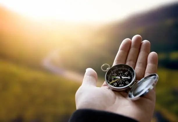 Photo of Traveler explorer man holding compass in a hand in mountains at sunrise, point of view.