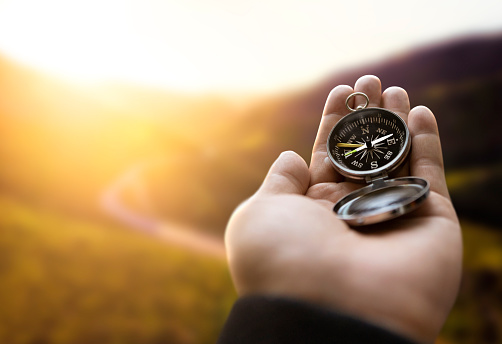 Traveler explorer man holding compass in a hand in mountains at sunrise, point of view.