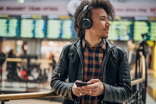 Young hispanic man using phone in shopping mall and listening music on headphone