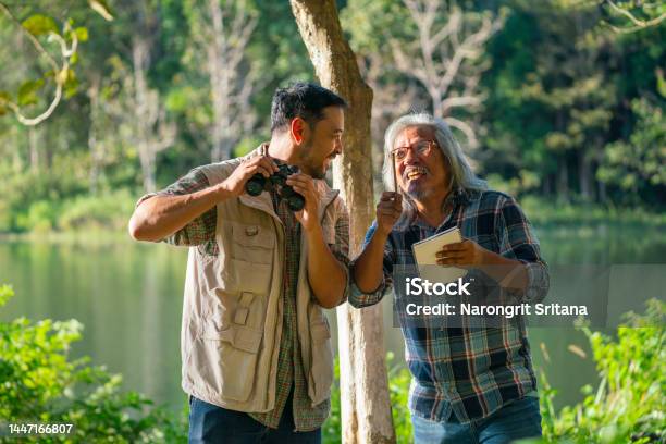 Front View Of Young Asian Man Hold Binoculars And Discuss With Senior Man Who Hold Book That Record Some Data And They Look Happy With Some New Finding Stock Photo - Download Image Now